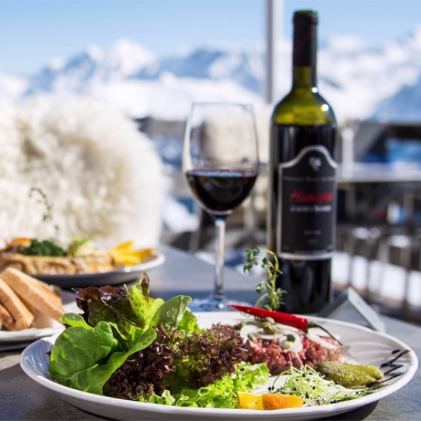 Fresh salad with red wine in Jackson Hole, Wyoming, overlooking snowy mountains. Membru links tourists to unique dining experiences.