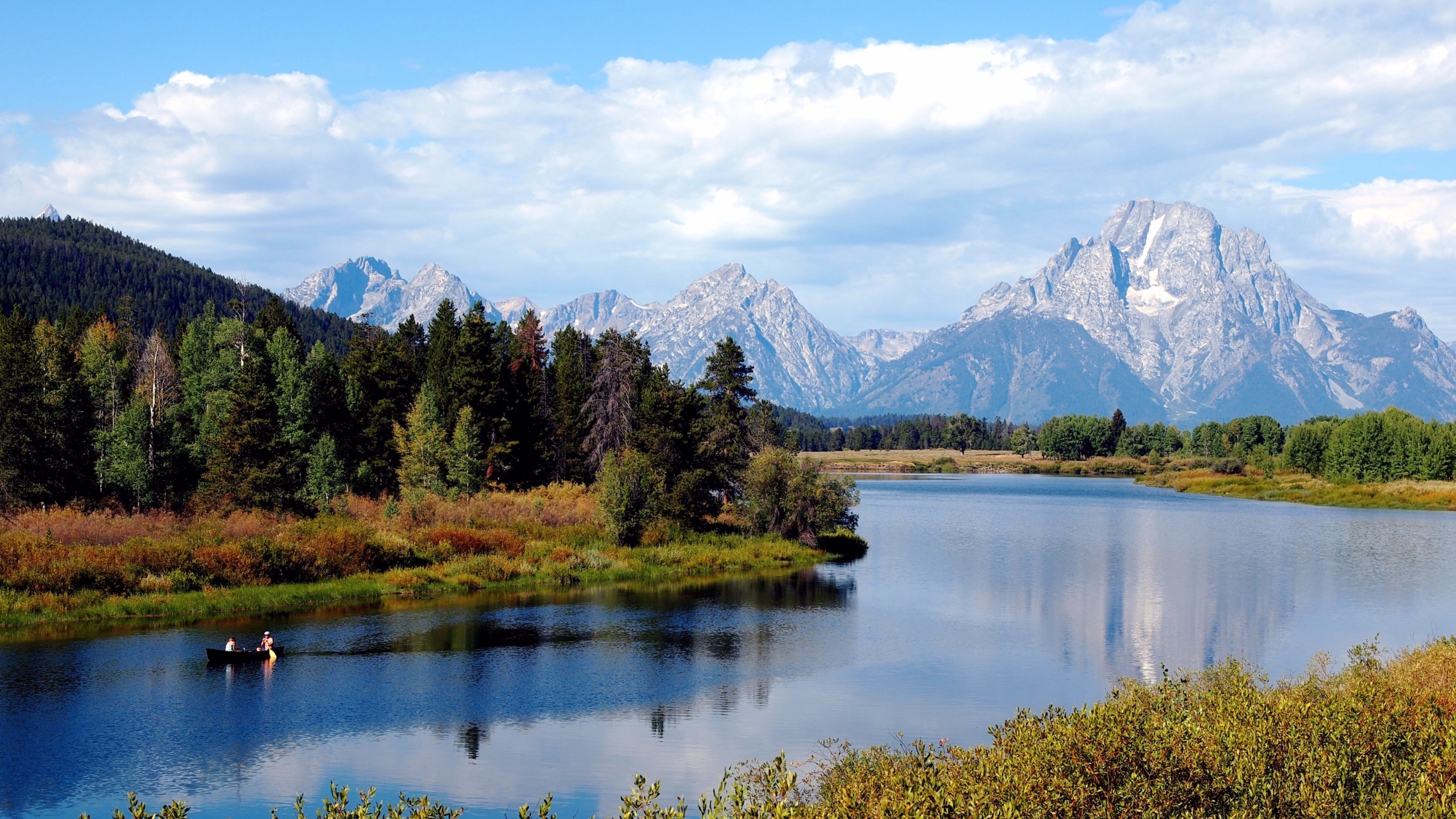 A serene scene of people canoeing on a calm lake with the majestic Teton Mountains and lush autumn trees in the background, Jackson Hole, Wyoming.